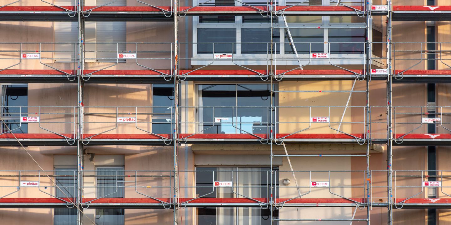 Fassadengerüst mit roten Belägen vor einer Wohnhausfassade im Abendlicht